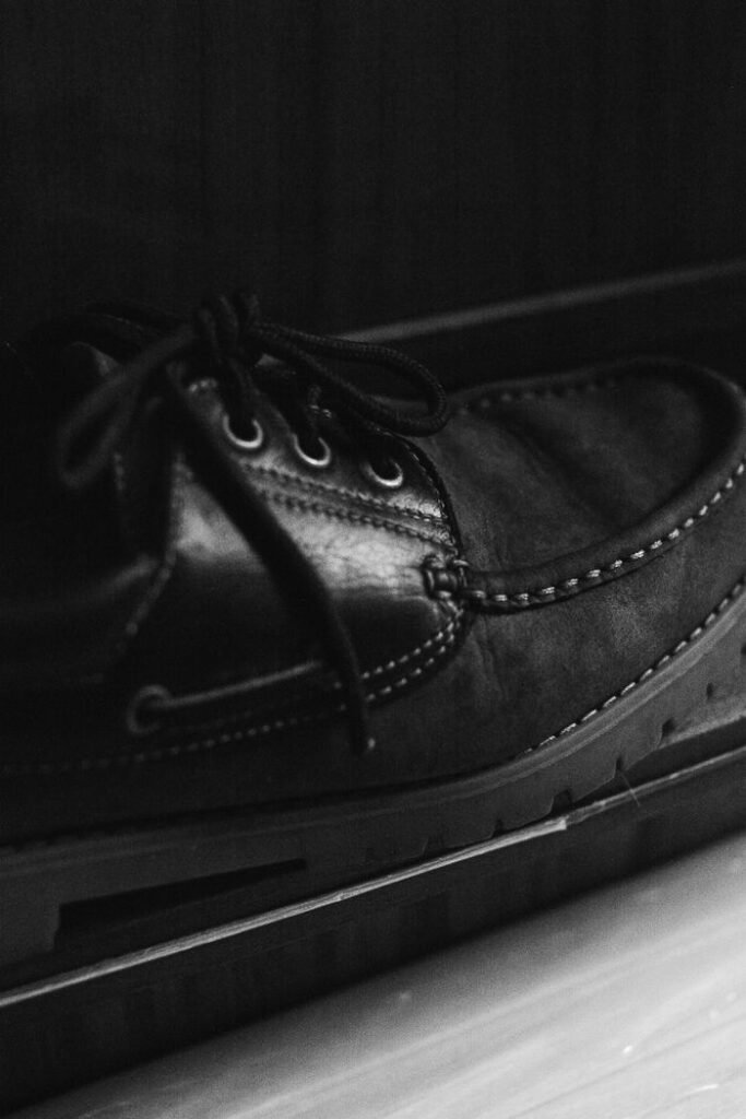 High contrast black and white close-up of a black leather shoe, emphasizing texture and detail.