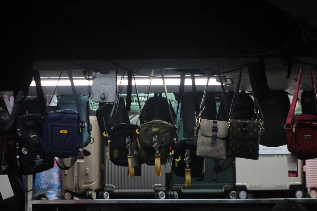 Colorful bags and luggage hang on display in a dimly lit market setting.