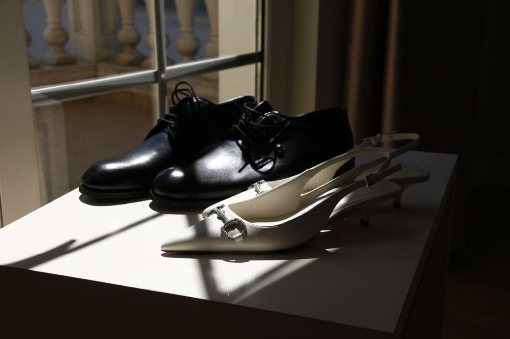 Close-up of stylish black men's and white women's shoes in sunlight by a window.