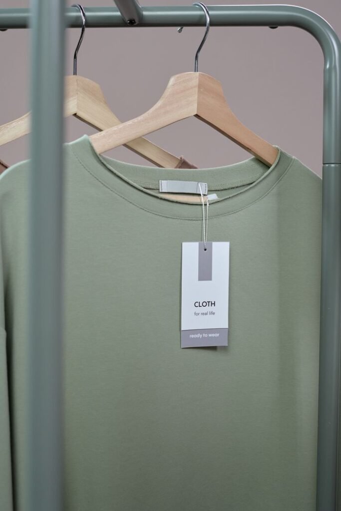 A simple green t-shirt with a tag hanging on a wooden hanger against a neutral background.